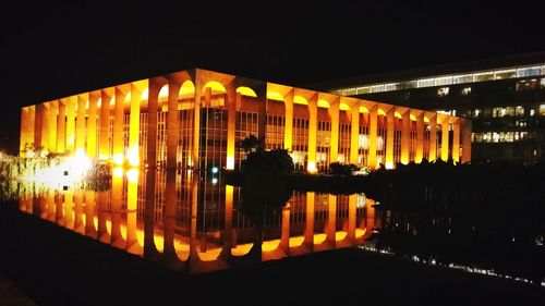 Illuminated buildings by lake against sky in city at night