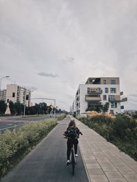 Rear view of people riding bicycle on road amidst buildings in city