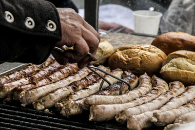 Cropped image of man holding sausage on barbecue grill