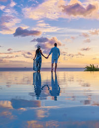 Rear view of woman standing at beach against sky during sunset