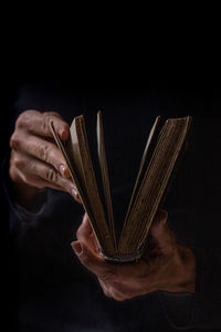 Close-up of human hand holding a book against black background
