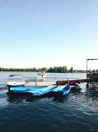 Boats moored on river against clear blue sky