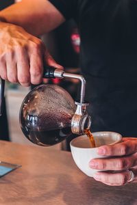 Cropped hands of man pouring coffee in cup at cafe