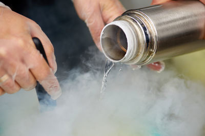 Cropped hands pouring liquid nitrogen from bottle