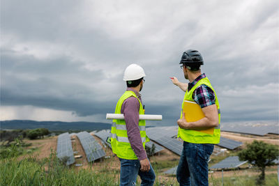 Side view of male colleagues discussing construction of solar power station on overcast day on site