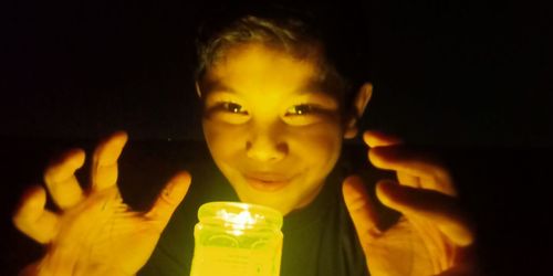 Close-up portrait of boy holding lit candle in the dark