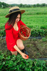 Portrait of young woman picking hat standing amidst plants