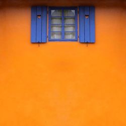 Full frame shot of orange house wall with blue window
