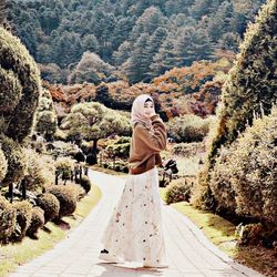 Rear view of woman standing on footpath amidst trees