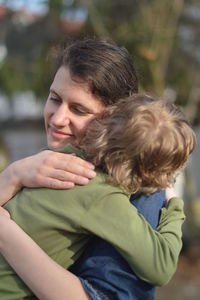 Happy mother holding little child in her arms with love in a garden outdoors in summertime