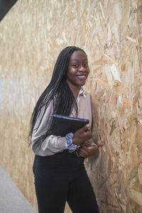 Smiling african american female entrepreneur standing with tablet near wall in coworking space while looking at camera