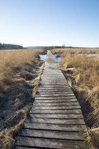 Boardwalk on field against clear sky