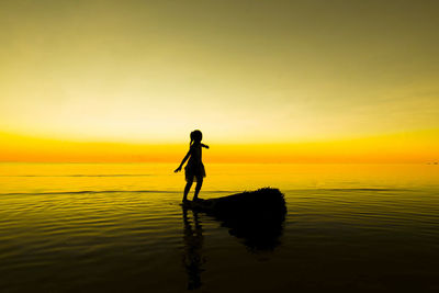 Silhouette man standing in sea against sky during sunset