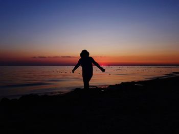 Silhouette man standing on beach against sky during sunset