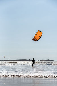Person paragliding on beach against clear sky