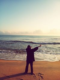 Rear view of man standing at beach against sky