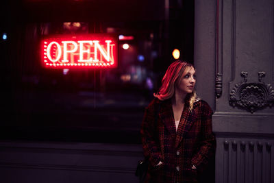 Young woman standing against illuminated wall at night