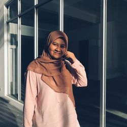 Portrait of smiling young woman standing against window