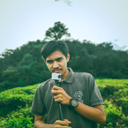 Young man holding camera while standing on field