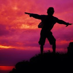 Low angle view of man with arms raised against cloudy sky