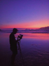 Silhouette man photographing sea against sky during sunset