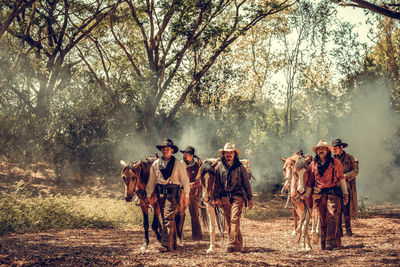 Men with horses walking on land in forest