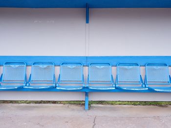 New blue metal seats on outdoor stadium players bench, chairs with blue paint below wooden roof.