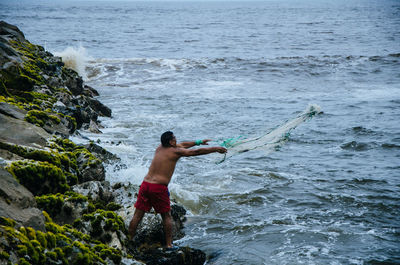 Shirtless man fishing in sea