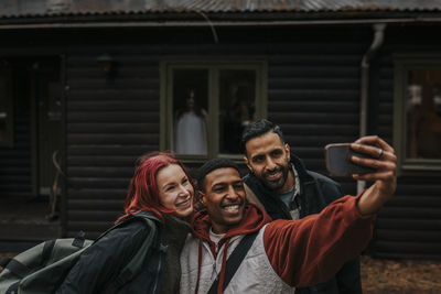 Happy multiracial friends taking selfie with smart phone while ghost at window in background