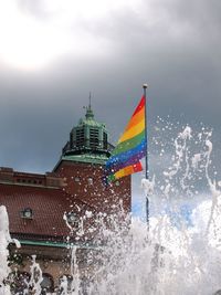 Rainbow flag amidst fountain against sky