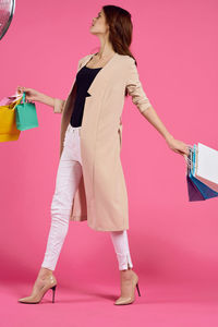Woman holding shopping bags while standing against pink background