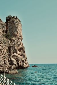 Rock formation in sea against clear sky