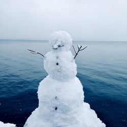 Frozen sea and snowman against sky during winter