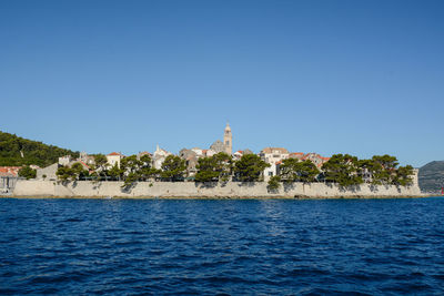 Buildings by sea against clear blue sky