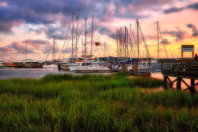 Sailboats moored in harbor at sunset