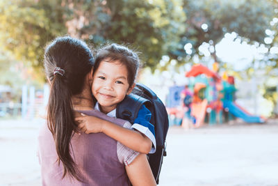 Rear view of mother carrying daughter while standing in playground