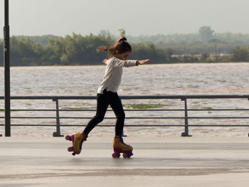 Girl roller skating on footpath against lake