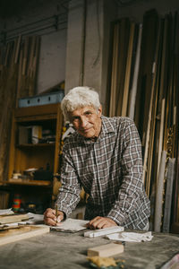 Portrait of senior male entrepreneur leaning on workbench at workshop