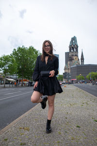 Full length portrait of young woman standing against sky in city