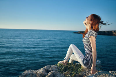 Woman sitting by sea against blue sky