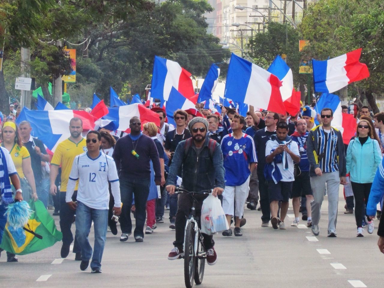 large group of people, flag, men, person, street, lifestyles, patriotism, walking, national flag, leisure activity, identity, road, multi colored, city, mixed age range, building exterior, city life, crowd, built structure