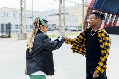 Happy friends greeting each other with fist bump on footpath