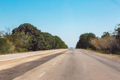 Empty road along trees and against sky