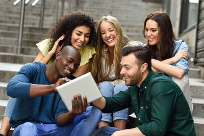 Smiling friends using digital tablet while sitting outdoors