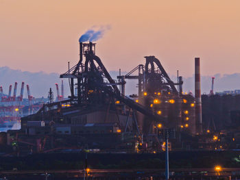 Illuminated factory against sky during sunset