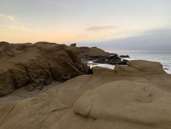 Rocks on beach against sky during sunset