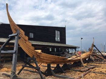 Abandoned wooden boat on field against cloudy sky