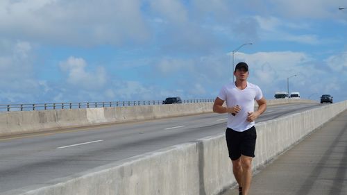 Young man jogging on road against sky