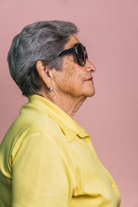 Side view of happy modern aged female with gray hair and in trendy sunglasses on pink background in studio and looking away