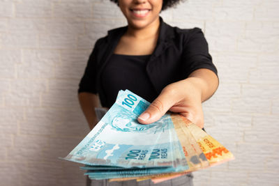 Young woman holding paper currency against wall